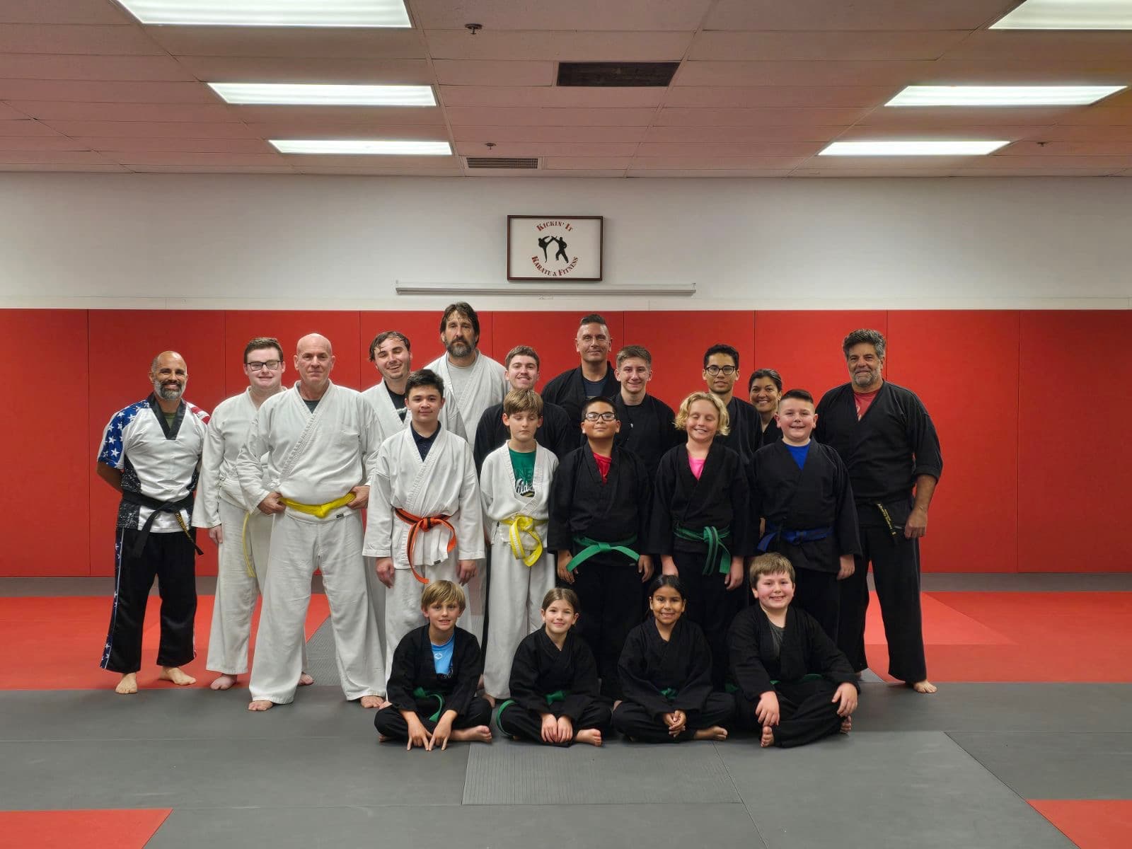 The full Kickin' It Karate & Fitness roster lined up by belt rank under the dojo sign